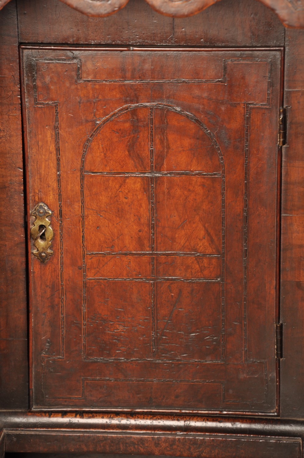 An early 18th-century walnut kneehole desk featuring crossbanded drawer fronts, brass drop handles, a central recessed cupboard, and turned bun feet. View XIX