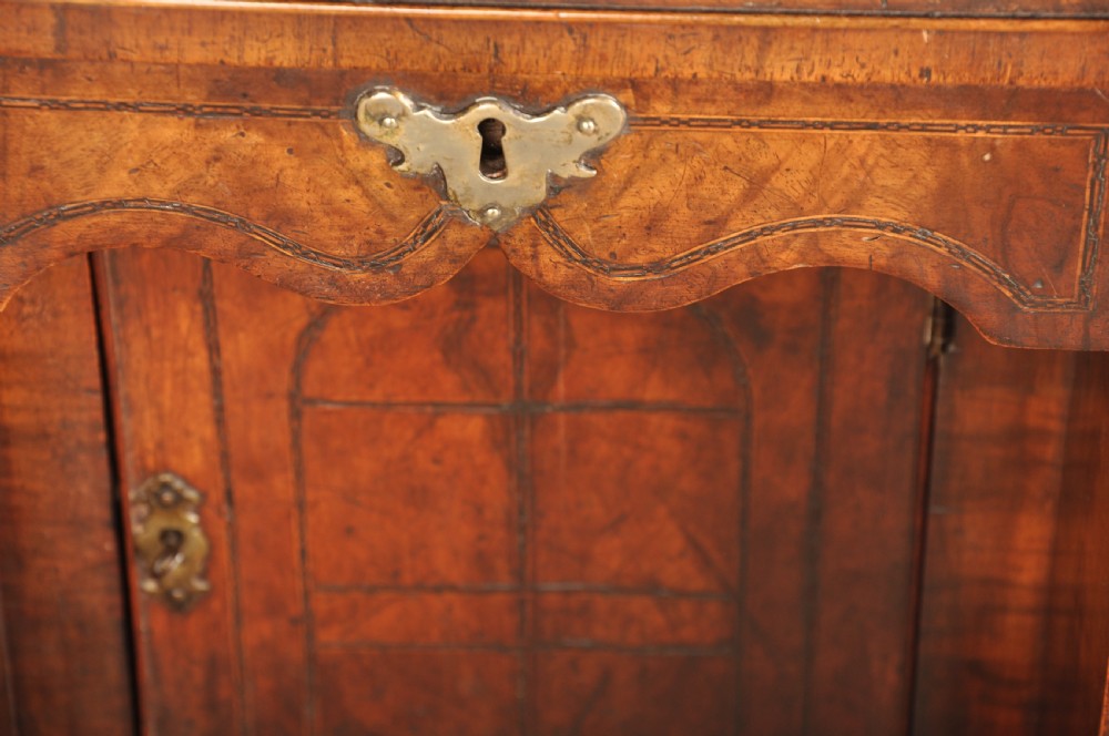 An early 18th-century walnut kneehole desk featuring crossbanded drawer fronts, brass drop handles, a central recessed cupboard, and turned bun feet. View XX