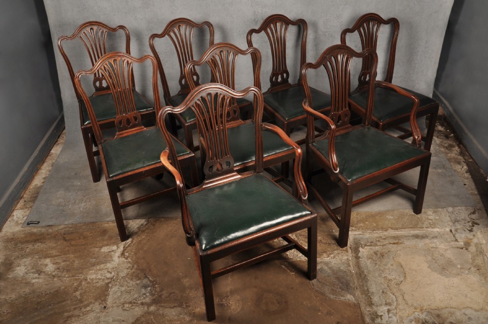 A set of eight 18th-century mahogany Hepplewhite dining chairs featuring pierced splat backrests, serpentine crest rails, square legs with stretchers, and dark green leather drop-in seats.