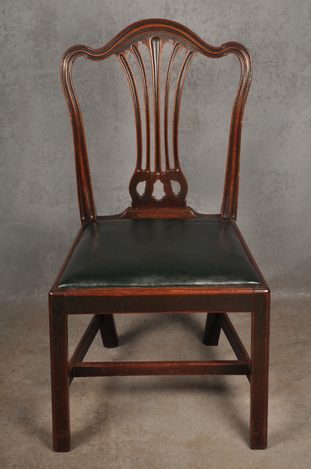 A set of eight 18th-century mahogany Hepplewhite dining chairs featuring pierced splat backrests, serpentine crest rails, square legs with stretchers, and dark green leather drop-in seats. View IV