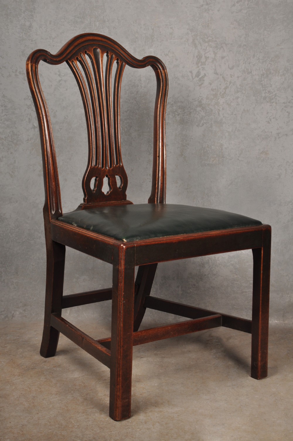 A set of eight 18th-century mahogany Hepplewhite dining chairs featuring pierced splat backrests, serpentine crest rails, square legs with stretchers, and dark green leather drop-in seats. View V