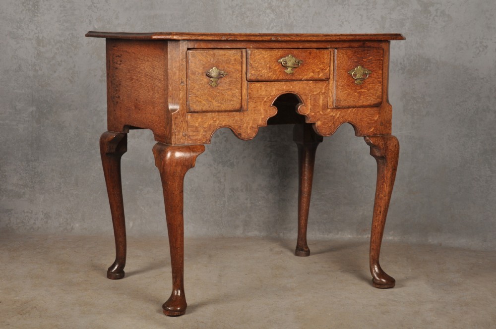 An early eighteenth-century oak lowboy side table featuring three drawers with brass handles, a shaped apron, and four cabriole legs with pad feet. View II