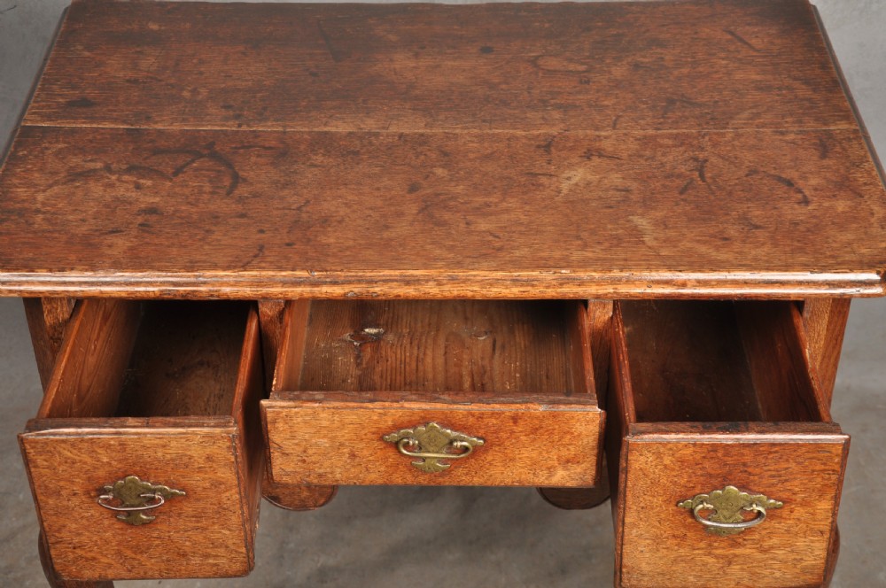 An early eighteenth-century oak lowboy side table featuring three drawers with brass handles, a shaped apron, and four cabriole legs with pad feet. View V