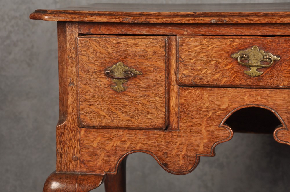 An early eighteenth-century oak lowboy side table featuring three drawers with brass handles, a shaped apron, and four cabriole legs with pad feet. View IX