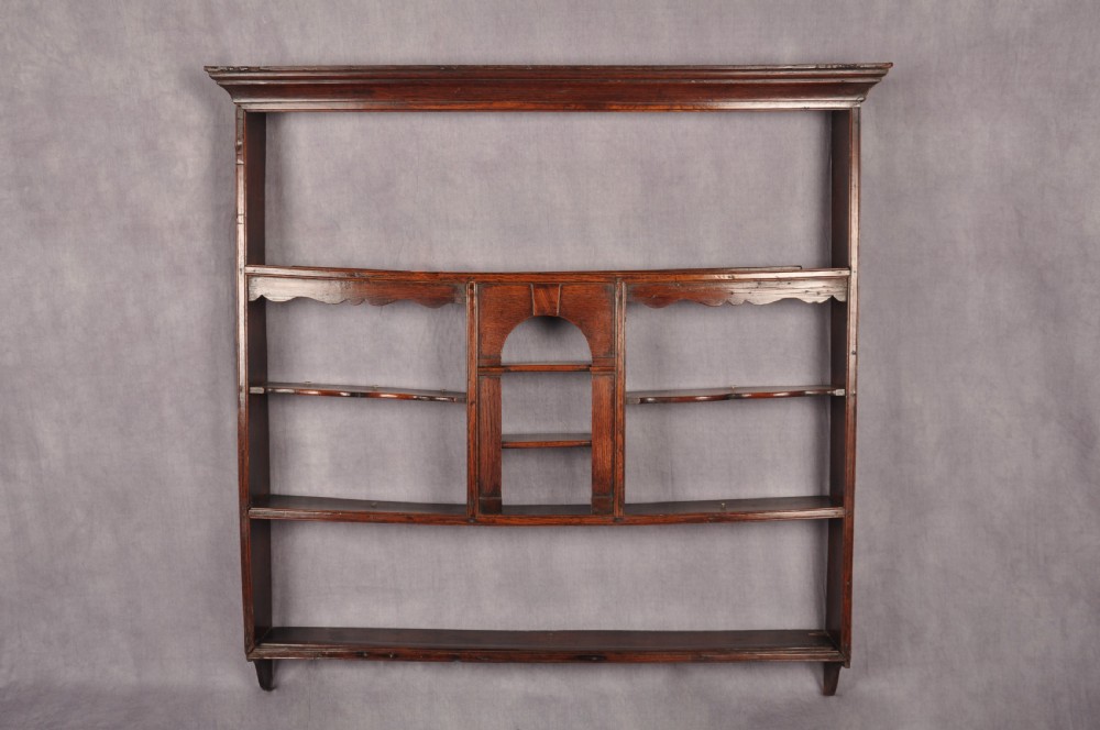 An eighteenth-century dark oak delft rack featuring open shelves, a central arched niche, and a moulded top cornice.