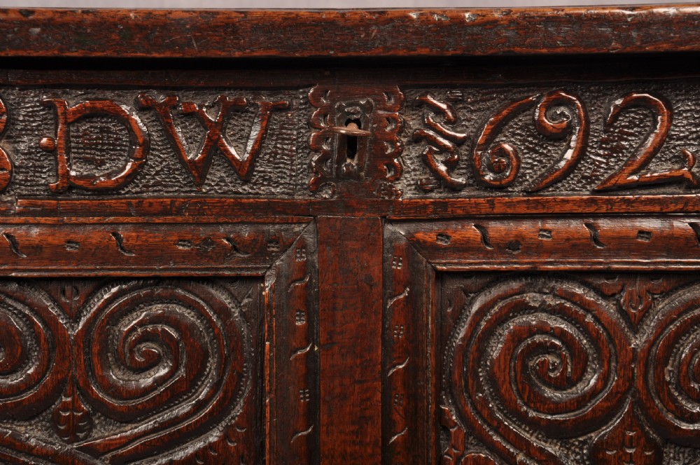 A seventeenth-century dark oak coffer featuring four carved front panels with scroll motifs, a carved top rail dated 1692 with initials DW, and a hinged lid. View II