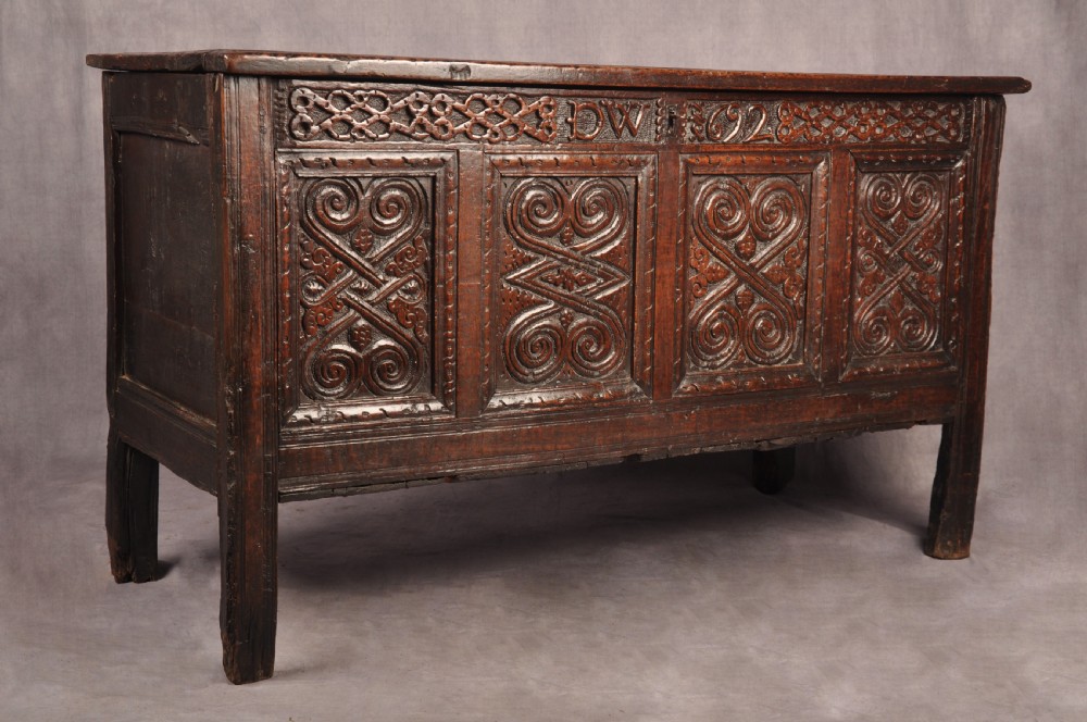 A seventeenth-century dark oak coffer featuring four carved front panels with scroll motifs, a carved top rail dated 1692 with initials DW, and a hinged lid. View III
