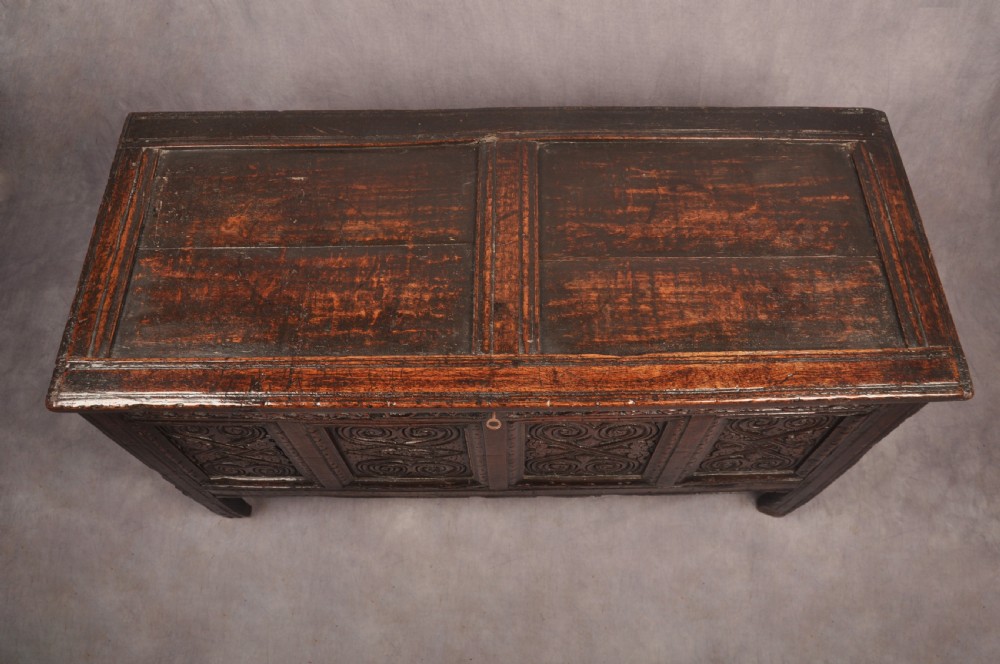 A seventeenth-century dark oak coffer featuring four carved front panels with scroll motifs, a carved top rail dated 1692 with initials DW, and a hinged lid. View VI
