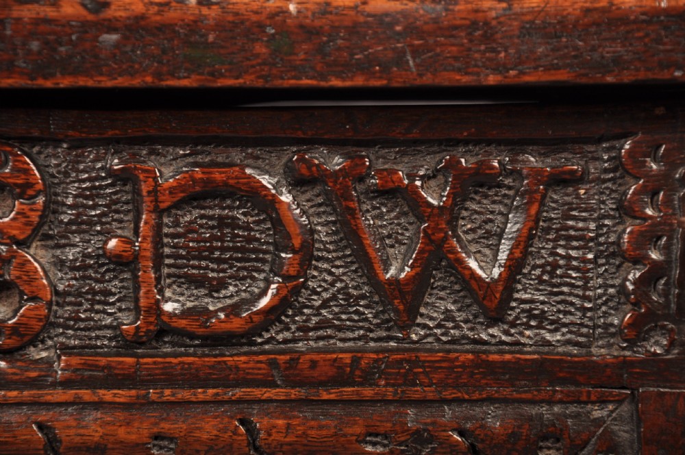 A seventeenth-century dark oak coffer featuring four carved front panels with scroll motifs, a carved top rail dated 1692 with initials DW, and a hinged lid. View VII