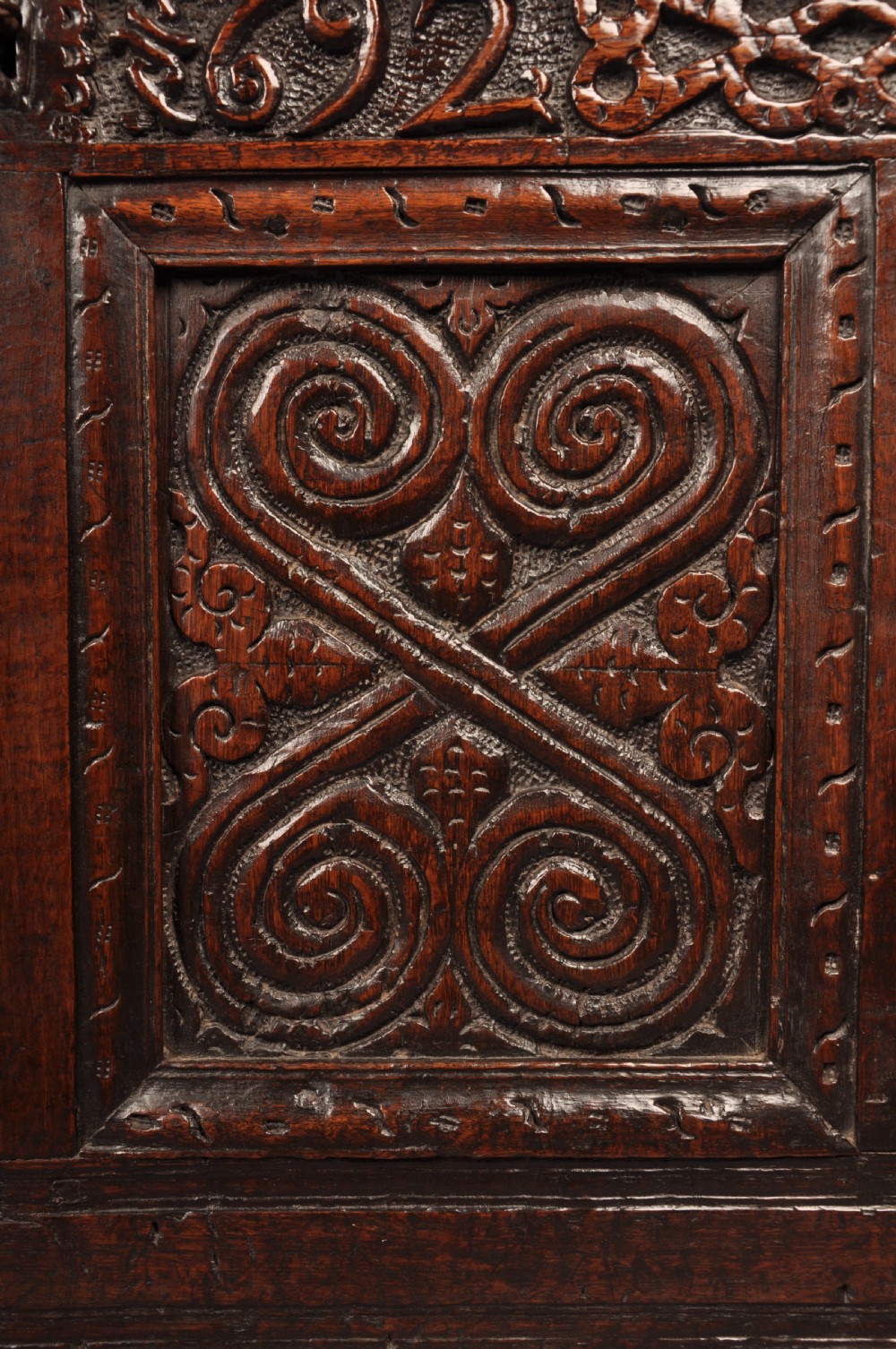 A seventeenth-century dark oak coffer featuring four carved front panels with scroll motifs, a carved top rail dated 1692 with initials DW, and a hinged lid. View VIII