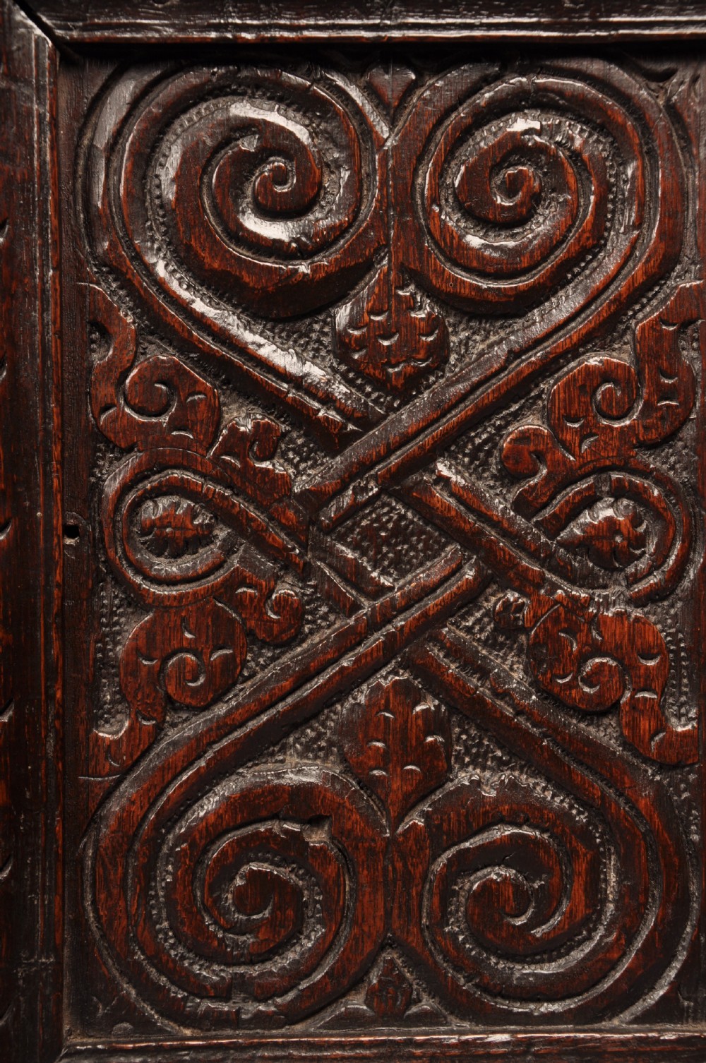 A seventeenth-century dark oak coffer featuring four carved front panels with scroll motifs, a carved top rail dated 1692 with initials DW, and a hinged lid. View IX