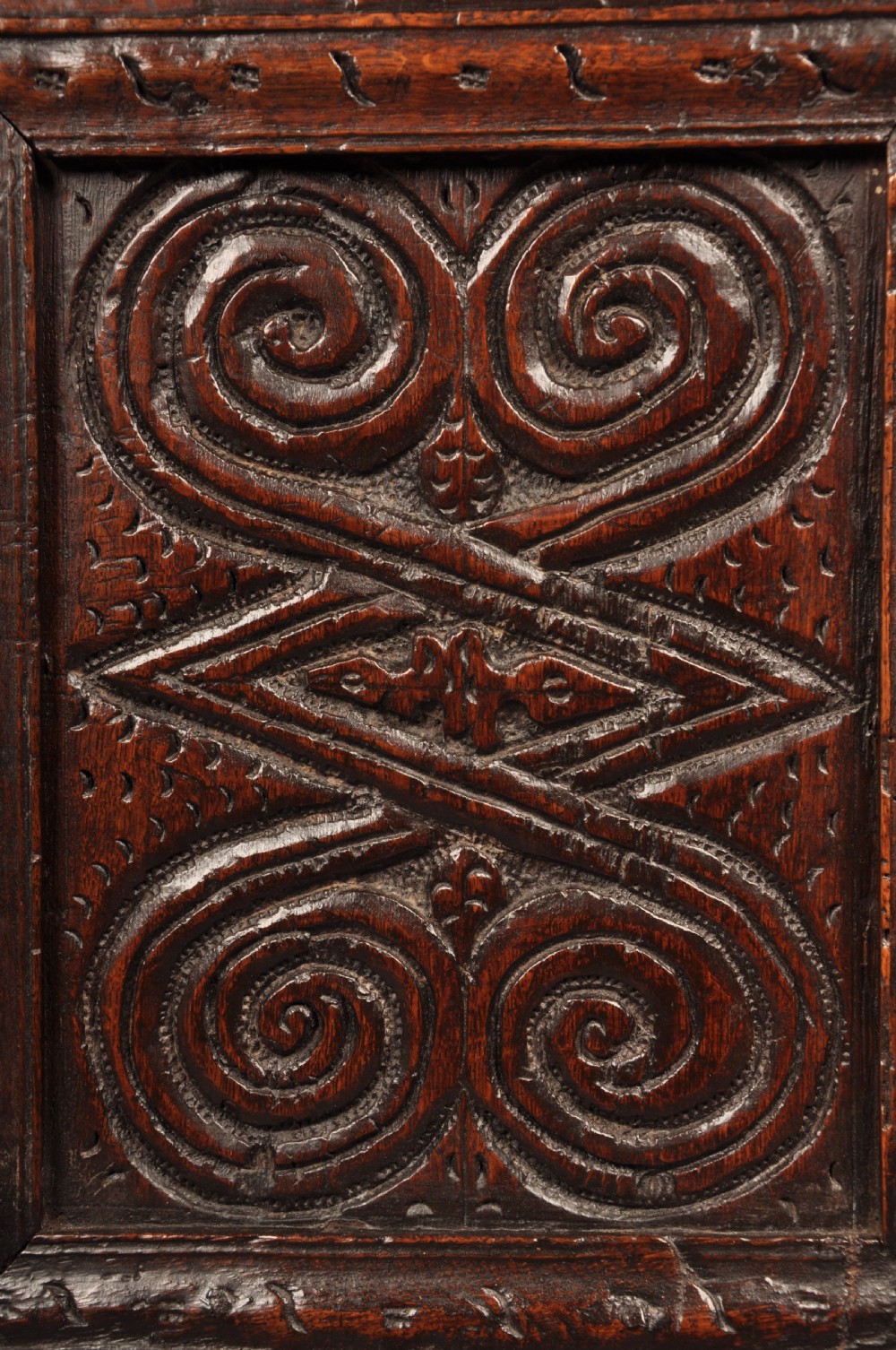 A seventeenth-century dark oak coffer featuring four carved front panels with scroll motifs, a carved top rail dated 1692 with initials DW, and a hinged lid. View X