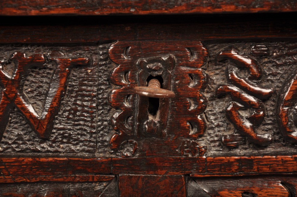 A seventeenth-century dark oak coffer featuring four carved front panels with scroll motifs, a carved top rail dated 1692 with initials DW, and a hinged lid. View XI