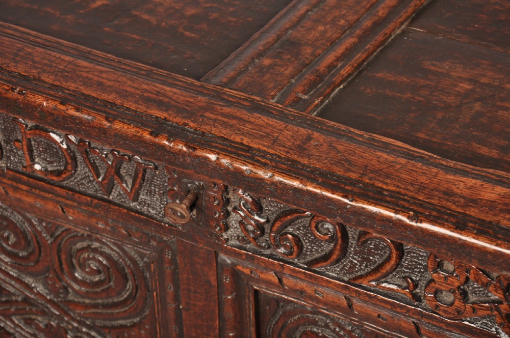 A seventeenth-century dark oak coffer featuring four carved front panels with scroll motifs, a carved top rail dated 1692 with initials DW, and a hinged lid. View XII