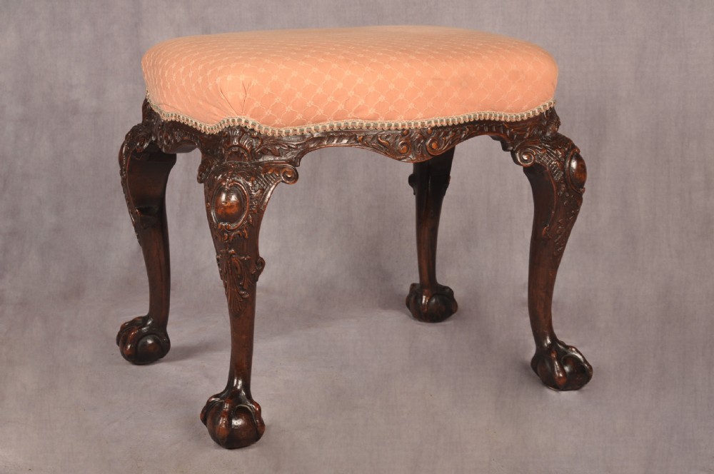A 19th-century carved walnut stool featuring cabriole legs with claw-and-ball feet and a peach patterned upholstered top.