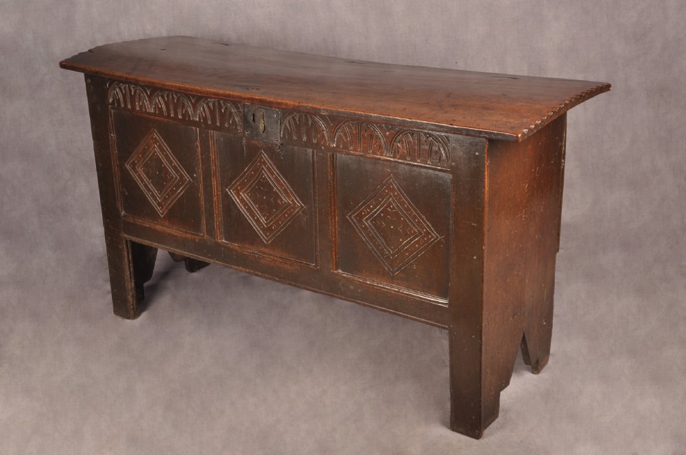 A dark oak 17th century coffer featuring carved lozenge motifs across three front panels beneath an arcaded frieze and iron lockplate.