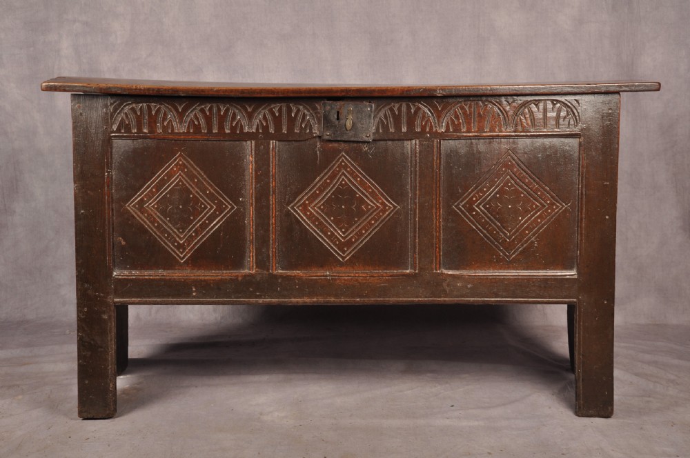 A dark oak 17th century coffer featuring carved lozenge motifs across three front panels beneath an arcaded frieze and iron lockplate. View II