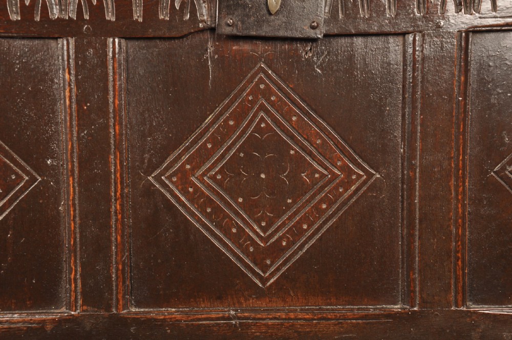 A dark oak 17th century coffer featuring carved lozenge motifs across three front panels beneath an arcaded frieze and iron lockplate. View III