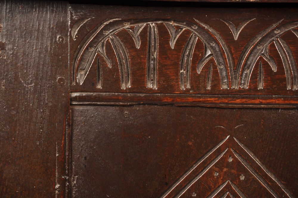 A dark oak 17th century coffer featuring carved lozenge motifs across three front panels beneath an arcaded frieze and iron lockplate. View V
