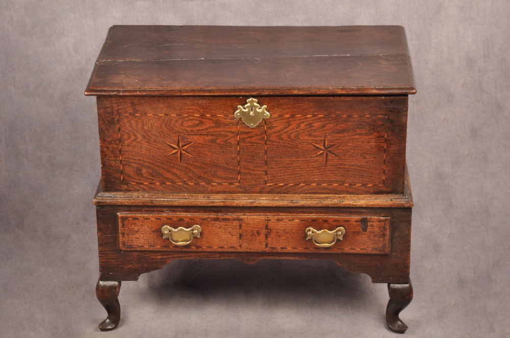 An early eighteenth-century oak coffer bach with star inlay details, a hinged top lid, a single lower drawer, and brass handles.