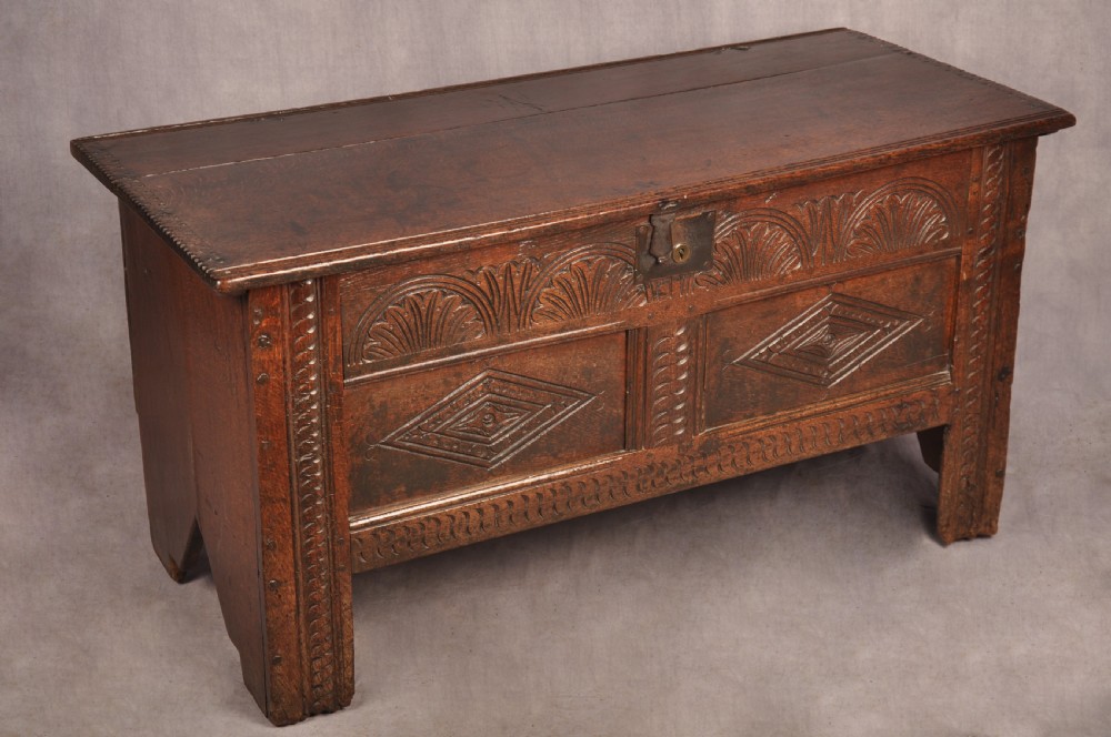 A small 17th-century dark oak coffer featuring carved lozenge and lunette patterns across the front with an iron escutcheon plate.