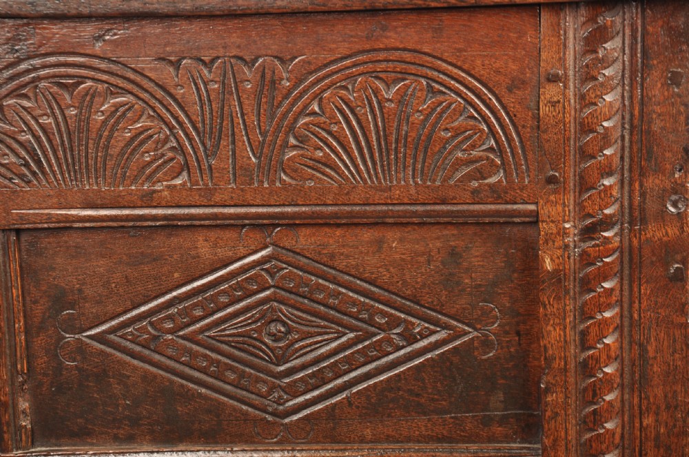 A small 17th-century dark oak coffer featuring carved lozenge and lunette patterns across the front with an iron escutcheon plate. View V