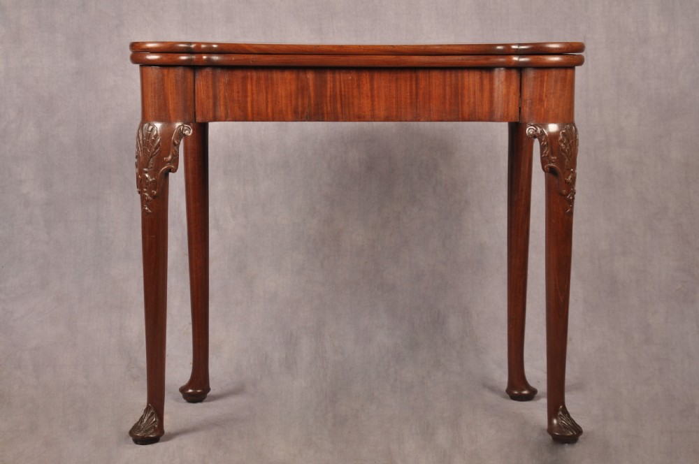 An 18th-century mahogany card table featuring a fold-over top, aproned frame, and carved cabriole legs.