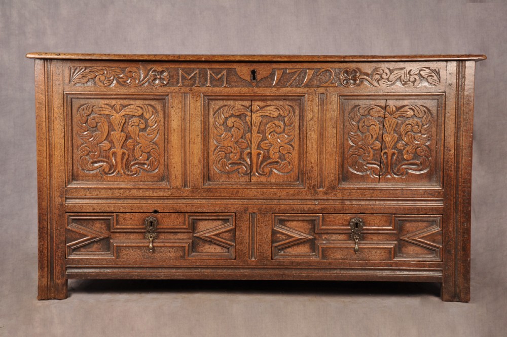 An 18th-century carved oak mule chest featuring three relief-carved front panels, a carved dated top frieze reading 1712, and two lower geometric drawers.