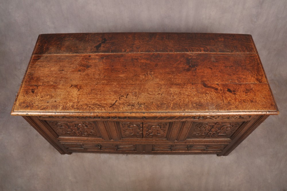 An 18th-century carved oak mule chest featuring three relief-carved front panels, a carved dated top frieze reading 1712, and two lower geometric drawers. View III