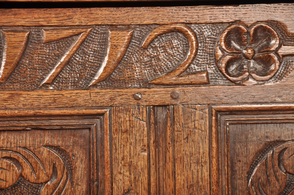 An 18th-century carved oak mule chest featuring three relief-carved front panels, a carved dated top frieze reading 1712, and two lower geometric drawers. View V