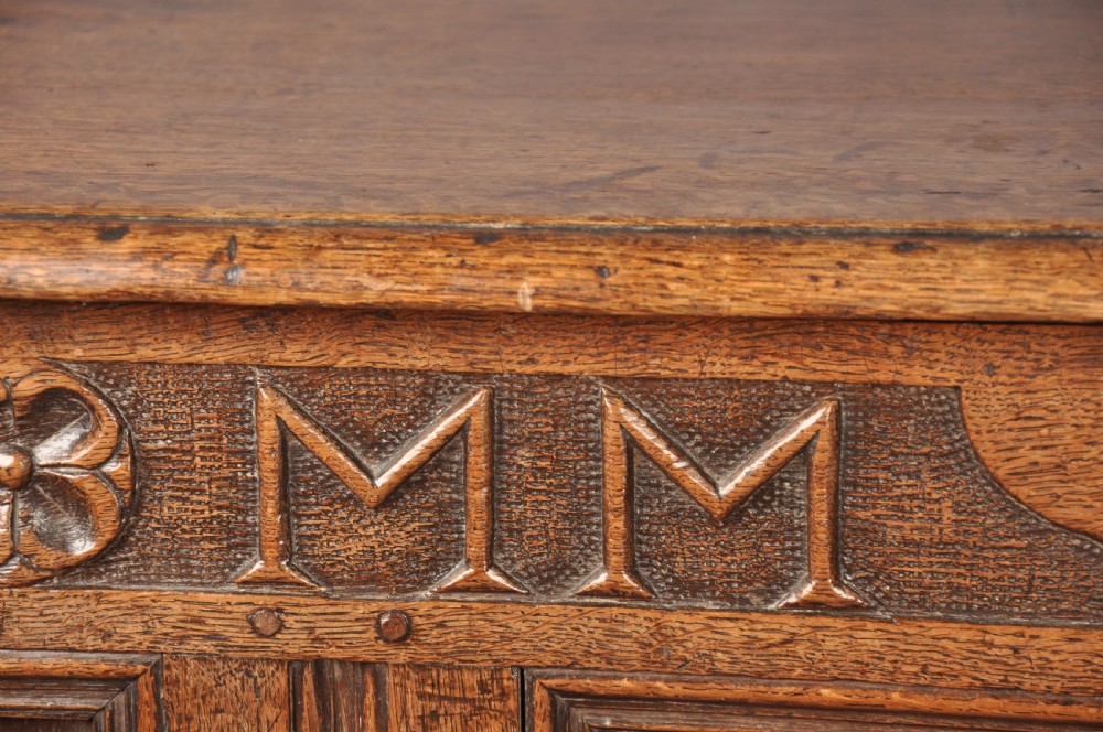 An 18th-century carved oak mule chest featuring three relief-carved front panels, a carved dated top frieze reading 1712, and two lower geometric drawers. View VI