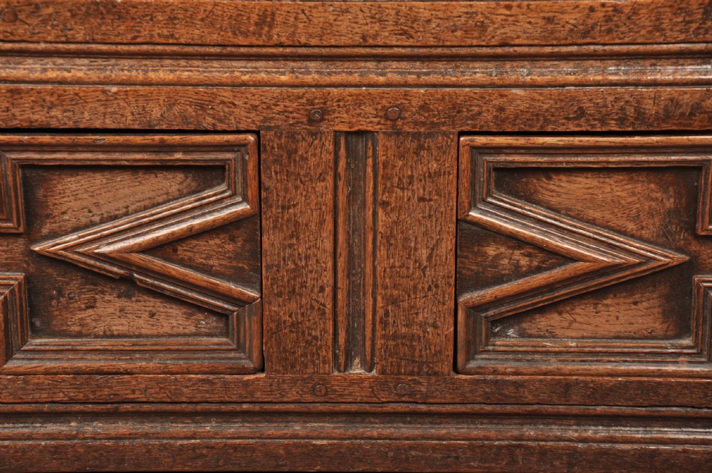 An 18th-century carved oak mule chest featuring three relief-carved front panels, a carved dated top frieze reading 1712, and two lower geometric drawers. View VII