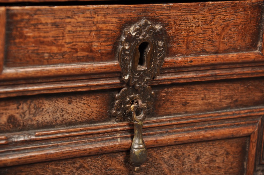 An 18th-century carved oak mule chest featuring three relief-carved front panels, a carved dated top frieze reading 1712, and two lower geometric drawers. View IX