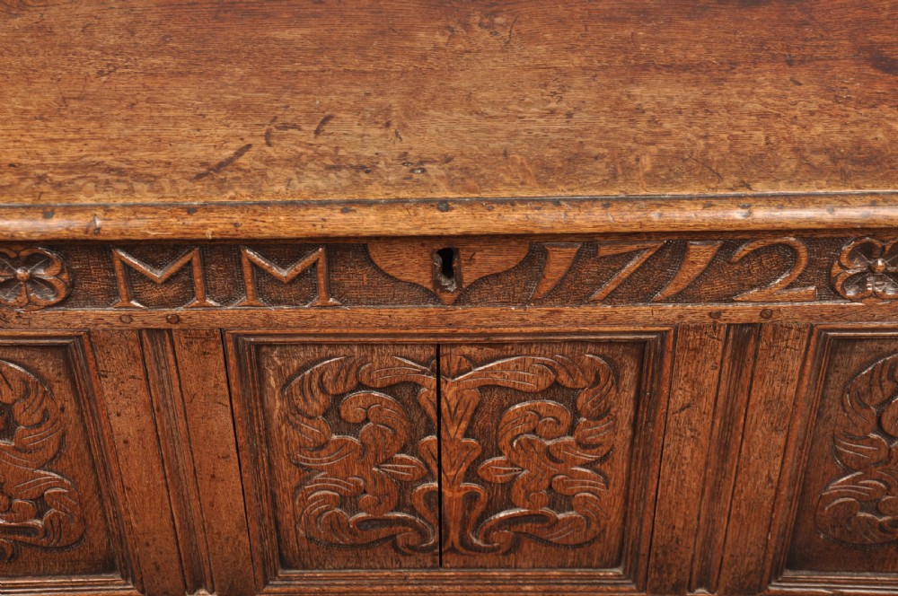 An 18th-century carved oak mule chest featuring three relief-carved front panels, a carved dated top frieze reading 1712, and two lower geometric drawers. View X