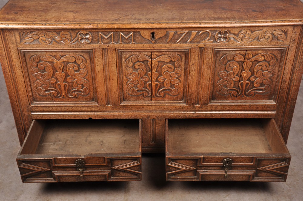 An 18th-century carved oak mule chest featuring three relief-carved front panels, a carved dated top frieze reading 1712, and two lower geometric drawers. View XI