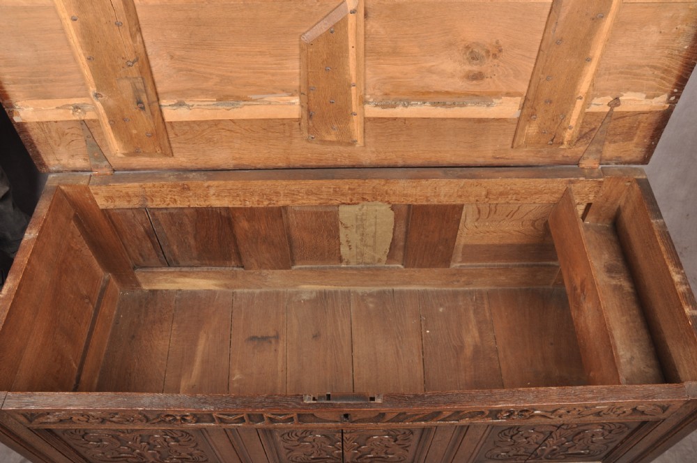An 18th-century carved oak mule chest featuring three relief-carved front panels, a carved dated top frieze reading 1712, and two lower geometric drawers. View XII
