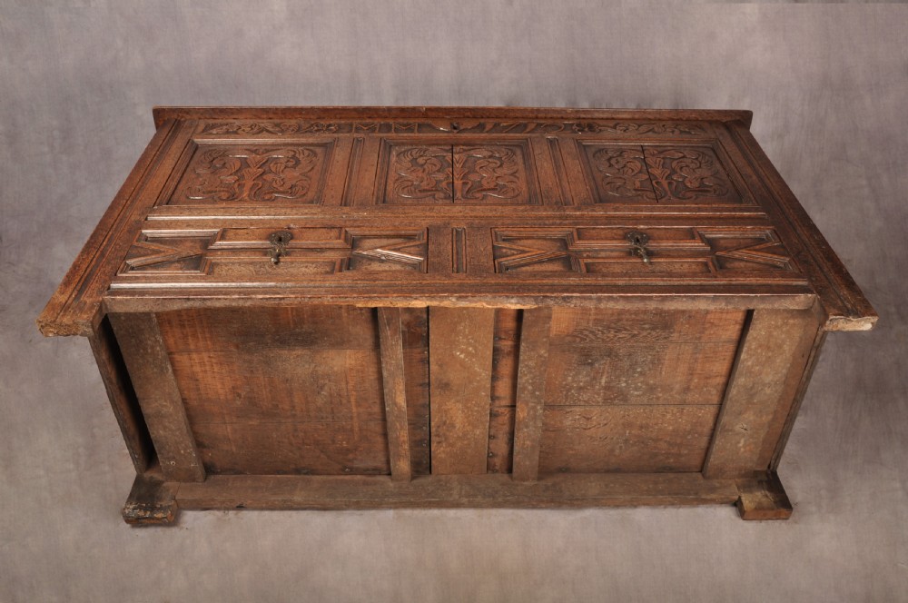 An 18th-century carved oak mule chest featuring three relief-carved front panels, a carved dated top frieze reading 1712, and two lower geometric drawers. View XIV
