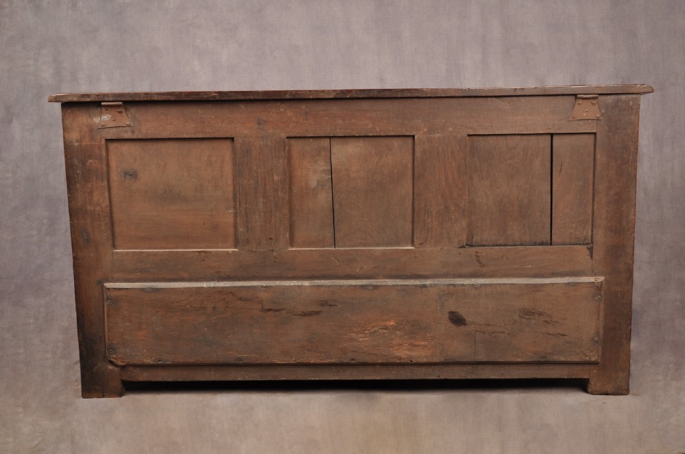 An 18th-century carved oak mule chest featuring three relief-carved front panels, a carved dated top frieze reading 1712, and two lower geometric drawers. View XVI
