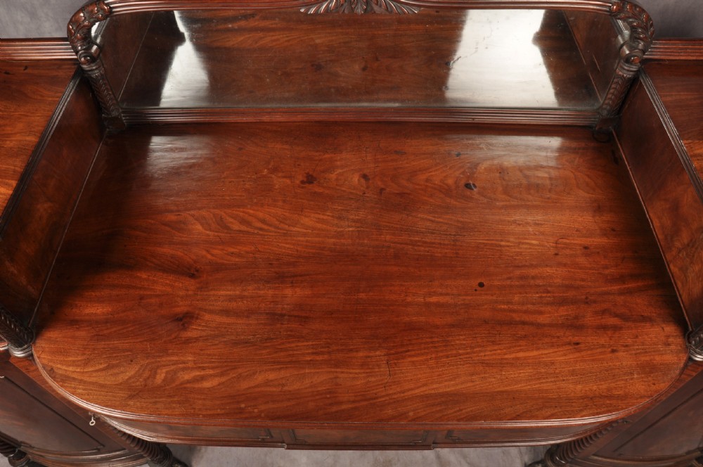 An antique Regency mahogany sideboard featuring flame mahogany panel doors, brass lion mask ring handles, spiral turned columns, hairy paw feet, and a central backboard mirror. View III