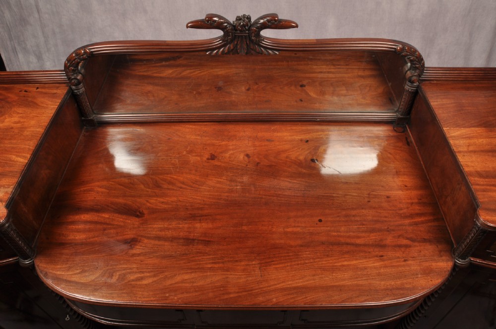 An antique Regency mahogany sideboard featuring flame mahogany panel doors, brass lion mask ring handles, spiral turned columns, hairy paw feet, and a central backboard mirror. View V