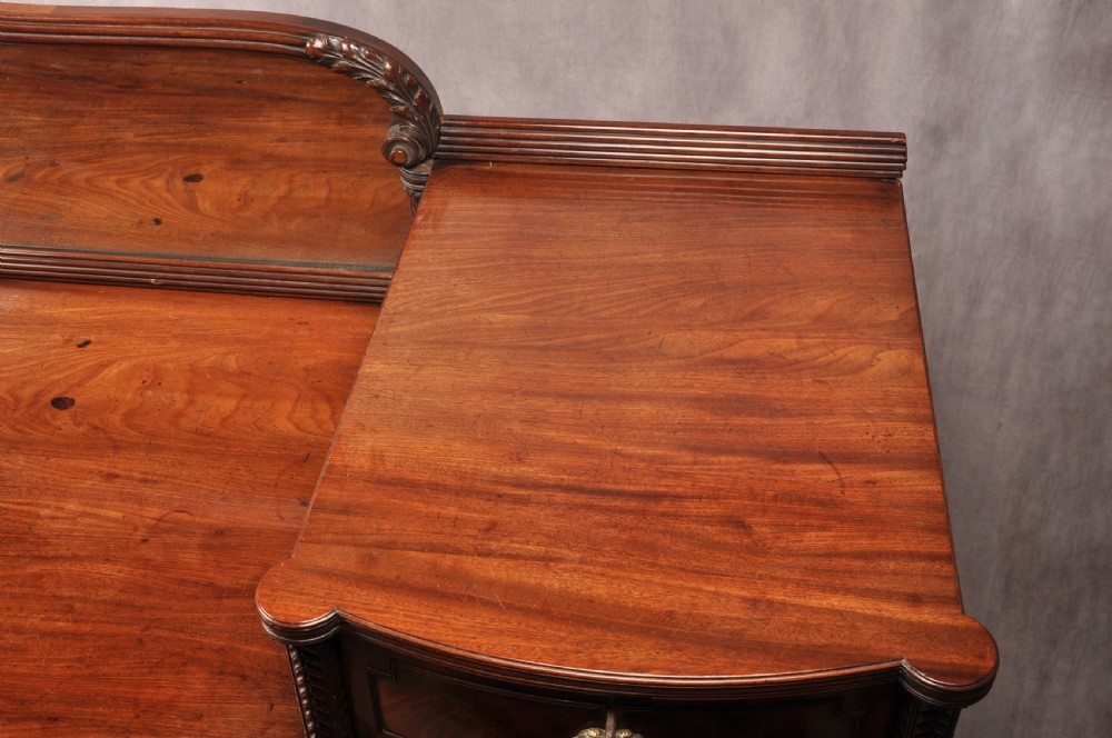 An antique Regency mahogany sideboard featuring flame mahogany panel doors, brass lion mask ring handles, spiral turned columns, hairy paw feet, and a central backboard mirror. View VIII