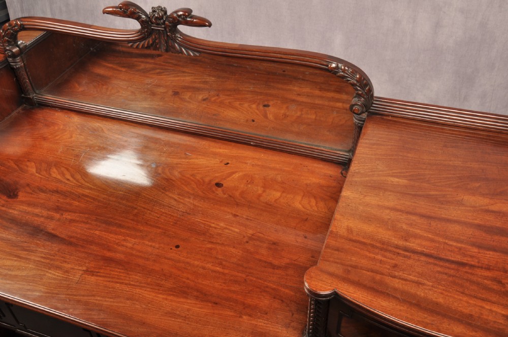 An antique Regency mahogany sideboard featuring flame mahogany panel doors, brass lion mask ring handles, spiral turned columns, hairy paw feet, and a central backboard mirror. View IX