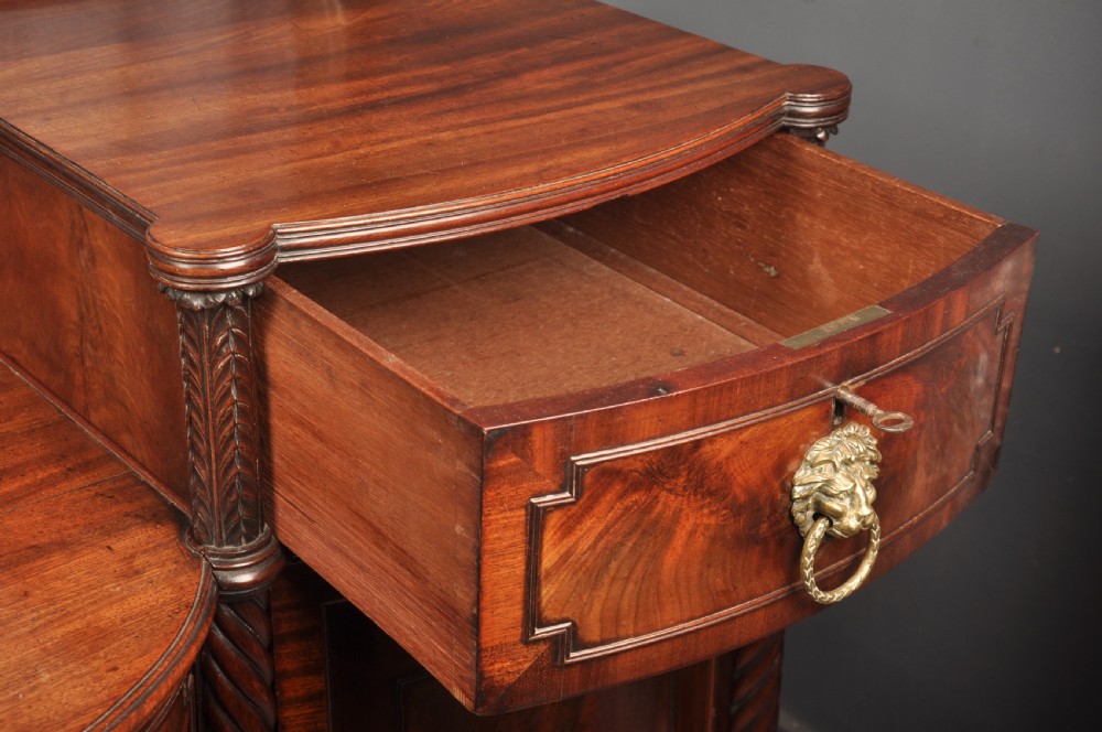 An antique Regency mahogany sideboard featuring flame mahogany panel doors, brass lion mask ring handles, spiral turned columns, hairy paw feet, and a central backboard mirror. View XIII