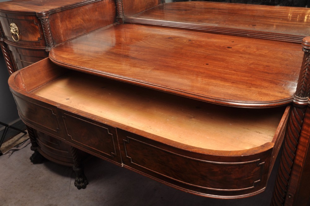 An antique Regency mahogany sideboard featuring flame mahogany panel doors, brass lion mask ring handles, spiral turned columns, hairy paw feet, and a central backboard mirror. View XIV