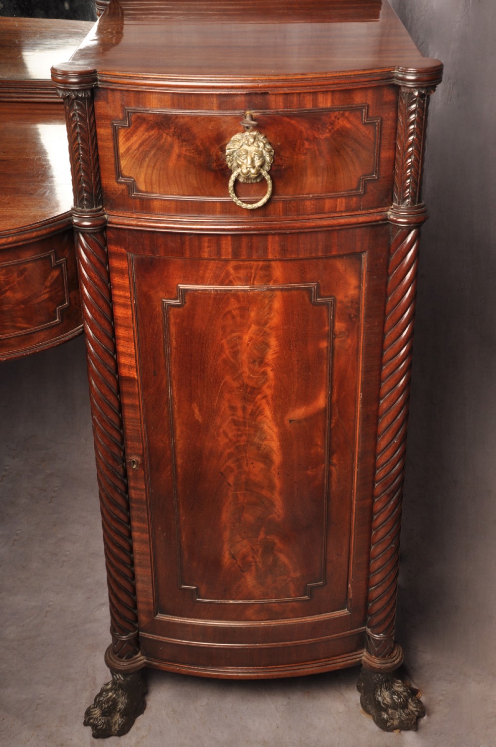 An antique Regency mahogany sideboard featuring flame mahogany panel doors, brass lion mask ring handles, spiral turned columns, hairy paw feet, and a central backboard mirror. View XVI