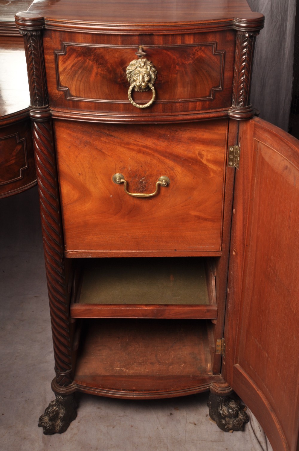 An antique Regency mahogany sideboard featuring flame mahogany panel doors, brass lion mask ring handles, spiral turned columns, hairy paw feet, and a central backboard mirror. View XIX