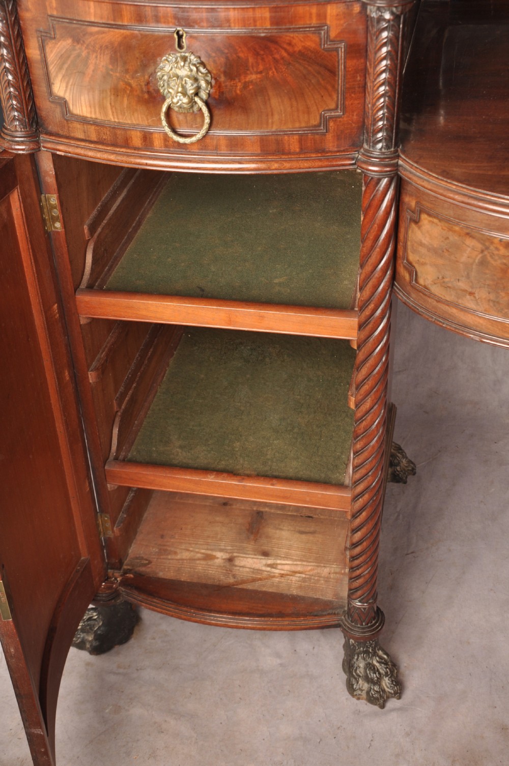 An antique Regency mahogany sideboard featuring flame mahogany panel doors, brass lion mask ring handles, spiral turned columns, hairy paw feet, and a central backboard mirror. View XX