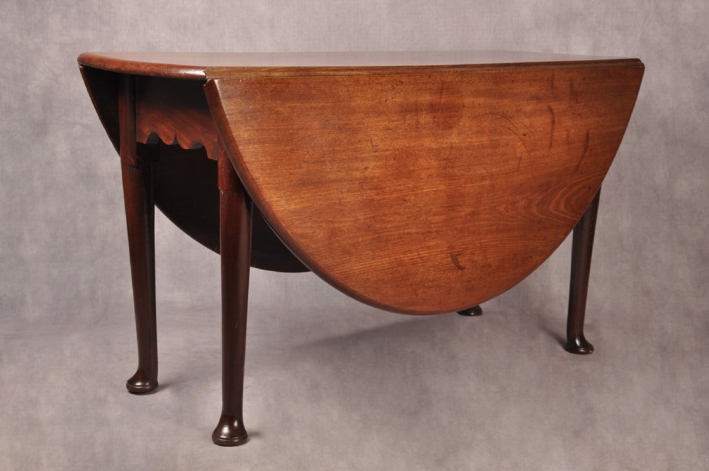 An 18th-century mahogany drop-leaf gateleg table with tapered legs, pad feet, and a scalloped apron on a plain background.