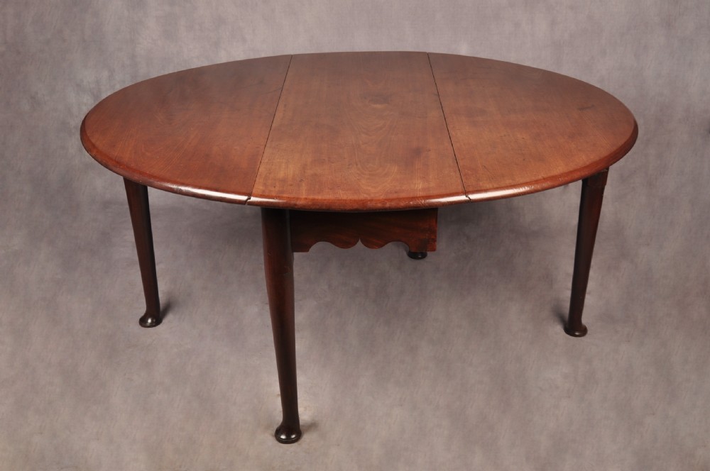 An 18th-century mahogany drop-leaf gateleg table with tapered legs, pad feet, and a scalloped apron on a plain background. View II