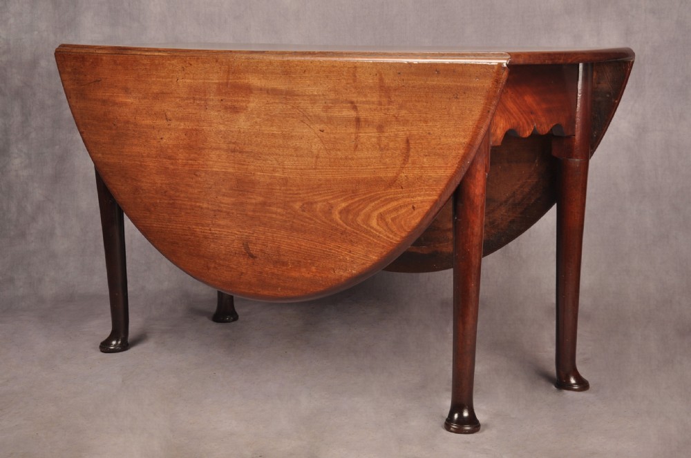 An 18th-century mahogany drop-leaf gateleg table with tapered legs, pad feet, and a scalloped apron on a plain background. View III
